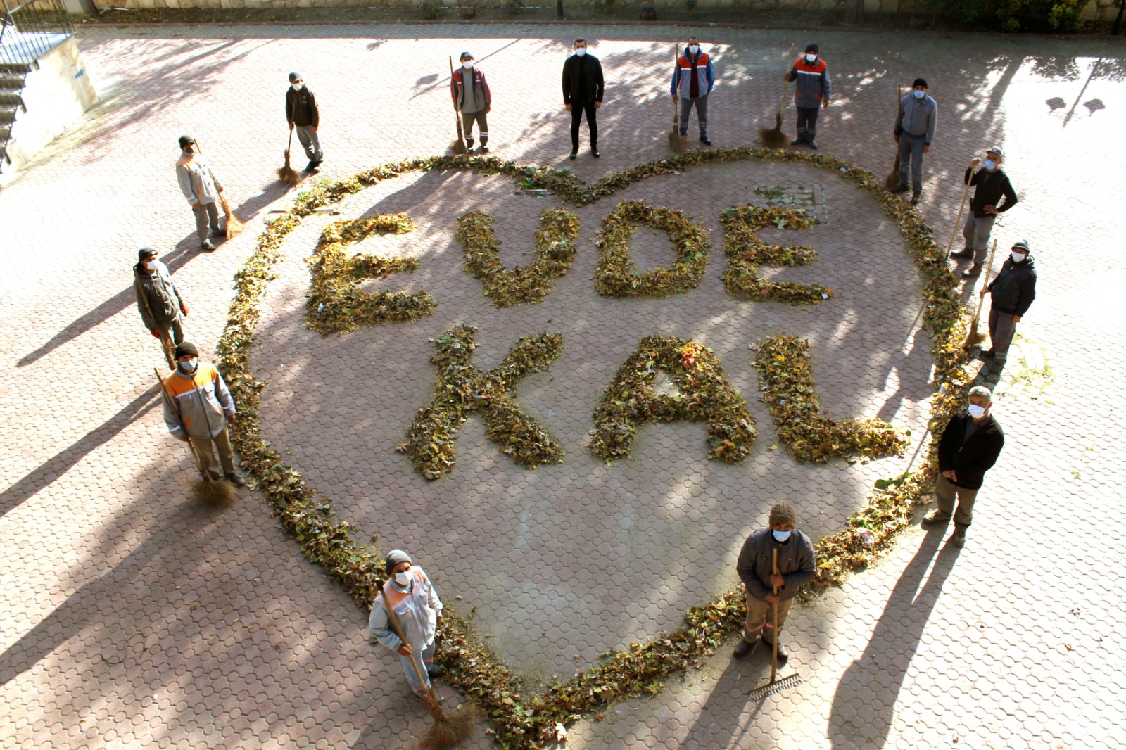 Temizlik işçileri ağaçlardan dökülen yapraklarla “Evde Kal” mesajı verdi